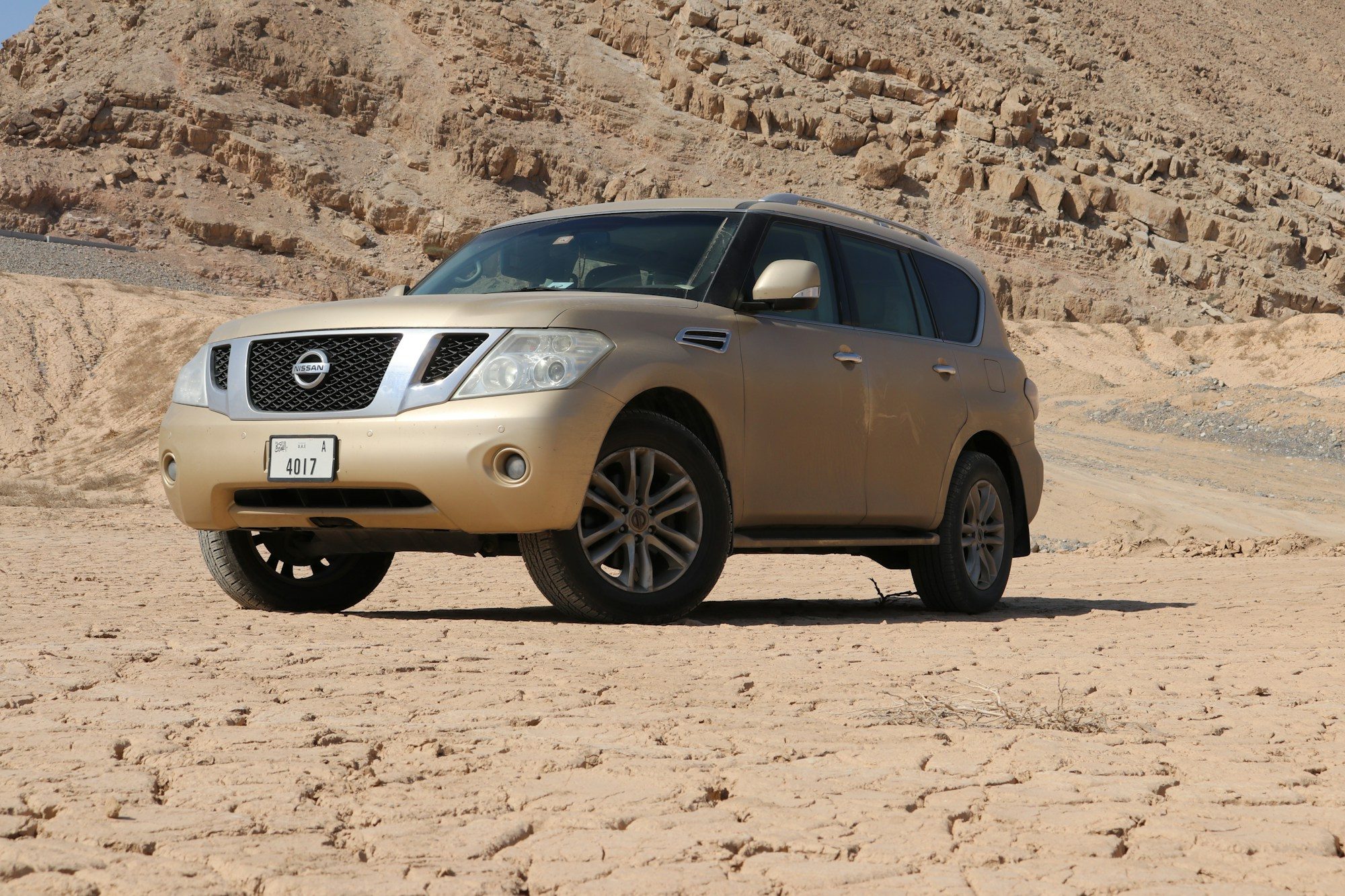 A gold early Nissan Patrol Y62 parked on cracked desert ground below rocky hills near Jebel Jais, Ras al Khaimah