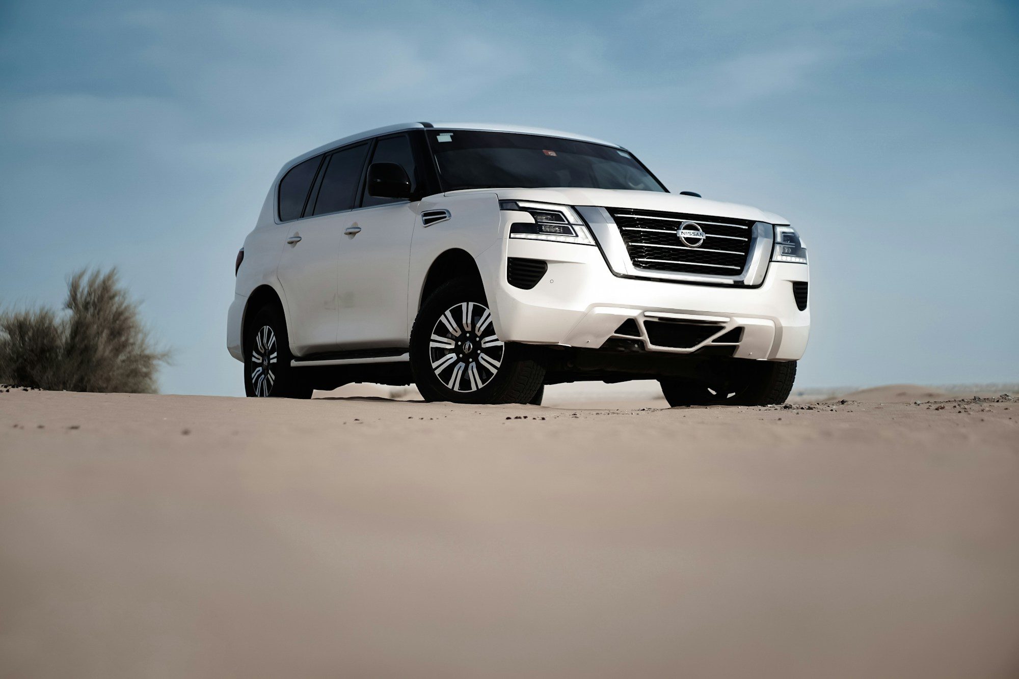 A white second-facelift Nissan Patrol Y62 parked on a sand flat under a blue sky