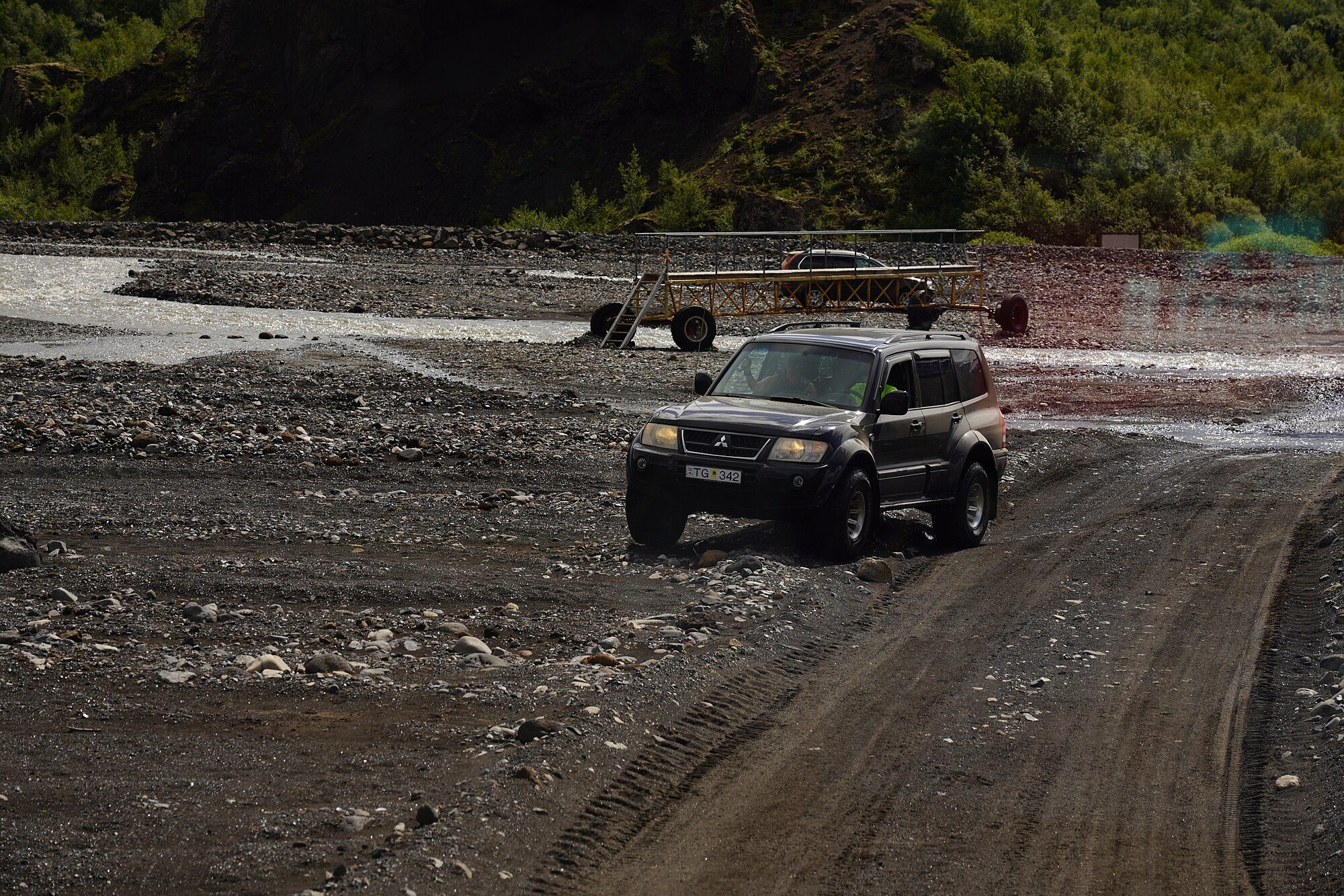 A lifted black facelifted third-generation Pajero on big tyres driving across gravel river flats in Iceland