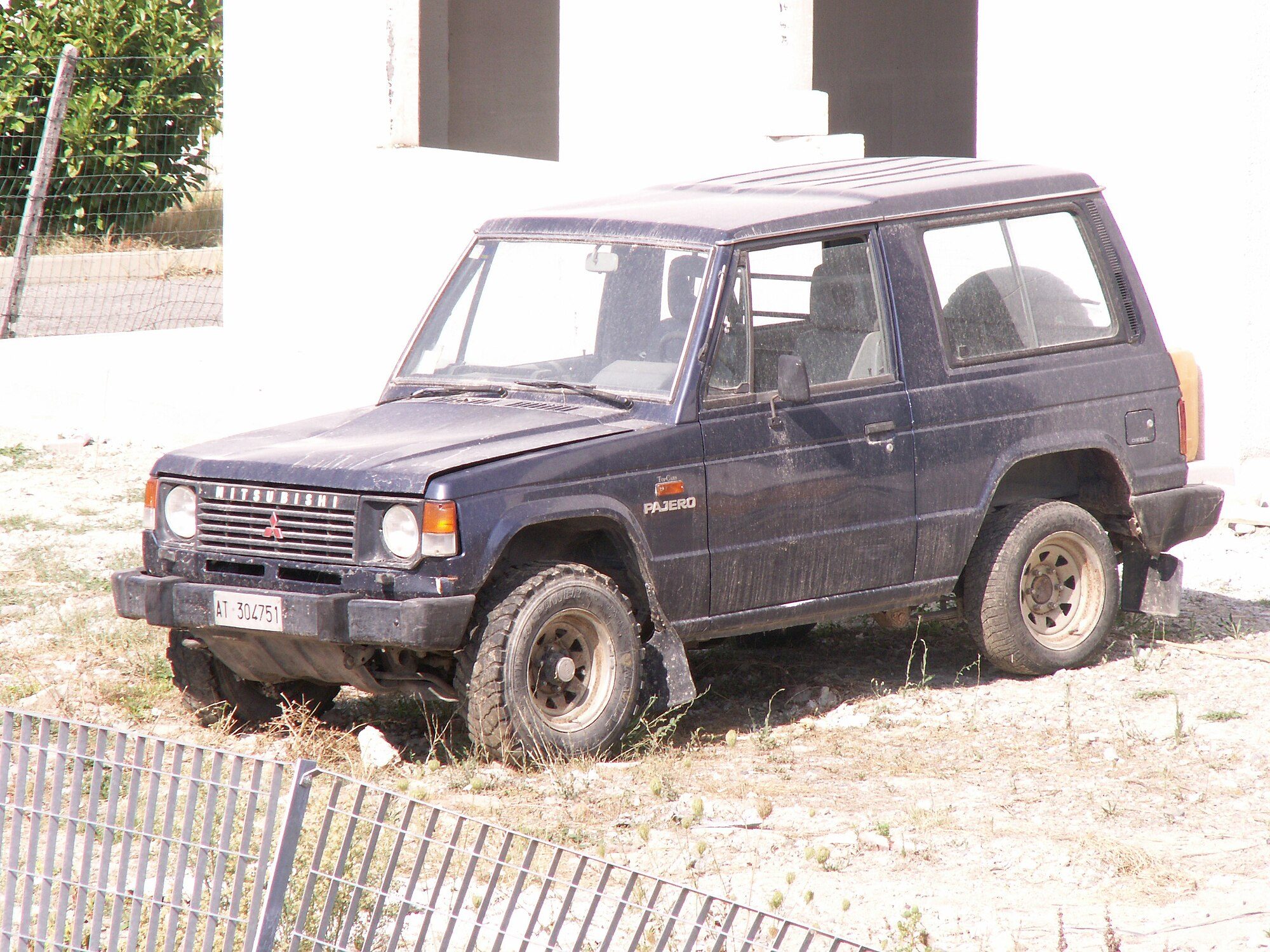 A dusty dark-blue first-generation short-wheelbase Pajero diesel parked on gravel and dry grass