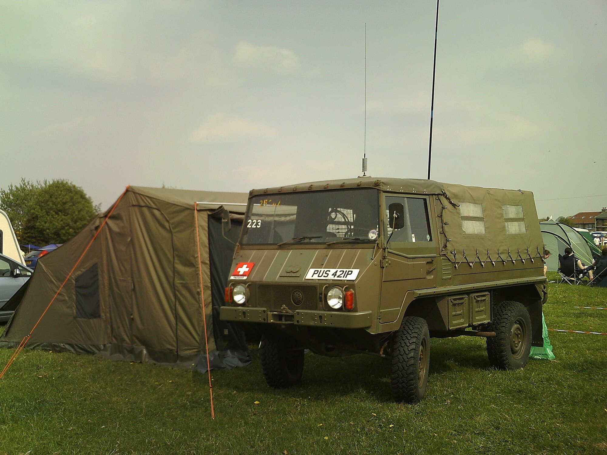 An ex-Swiss Army Pinzgauer 710M soft top parked beside a canvas tent on a grassy campsite