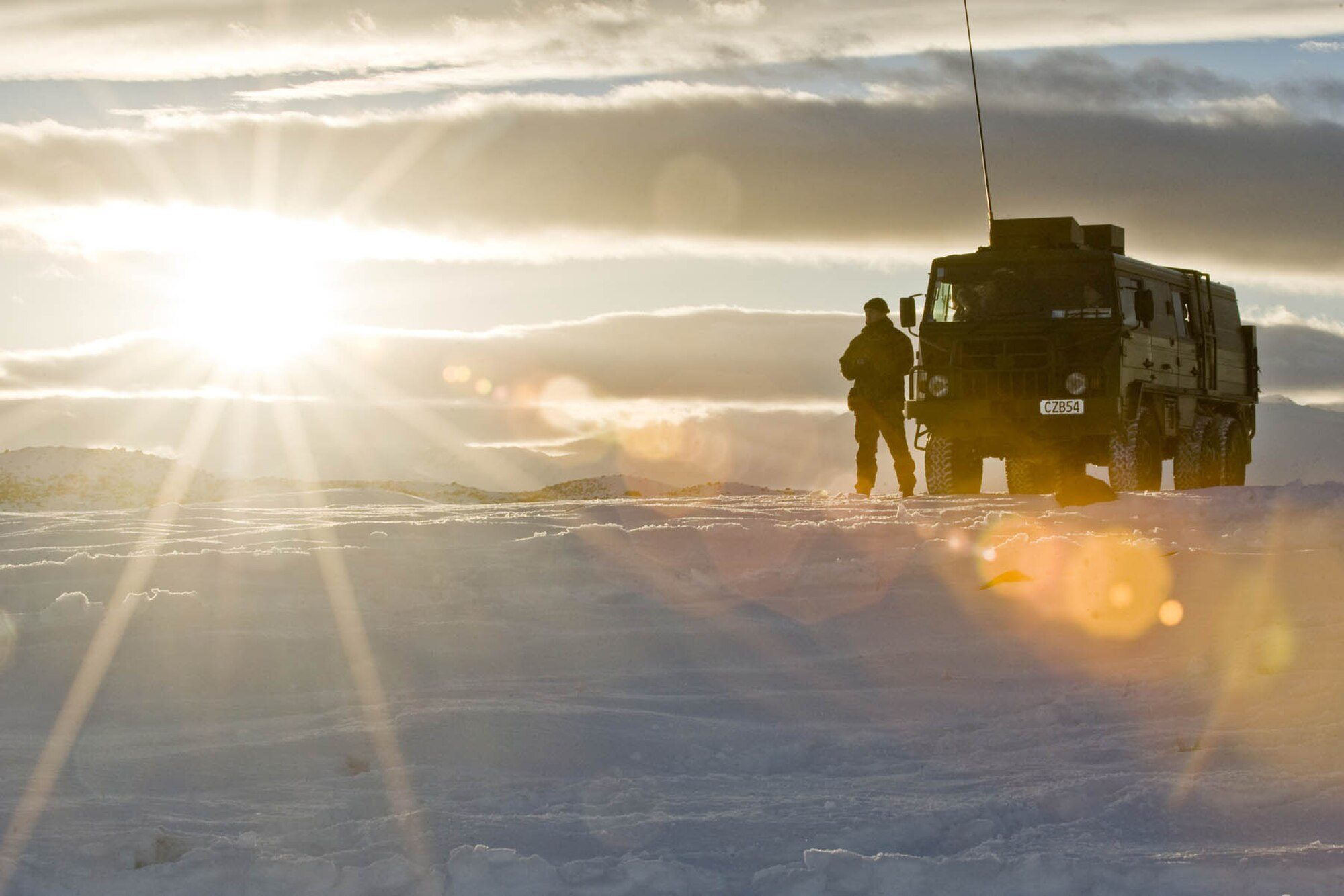 A soldier stands beside a box-bodied Pinzgauer 718 on a snowfield at sunrise