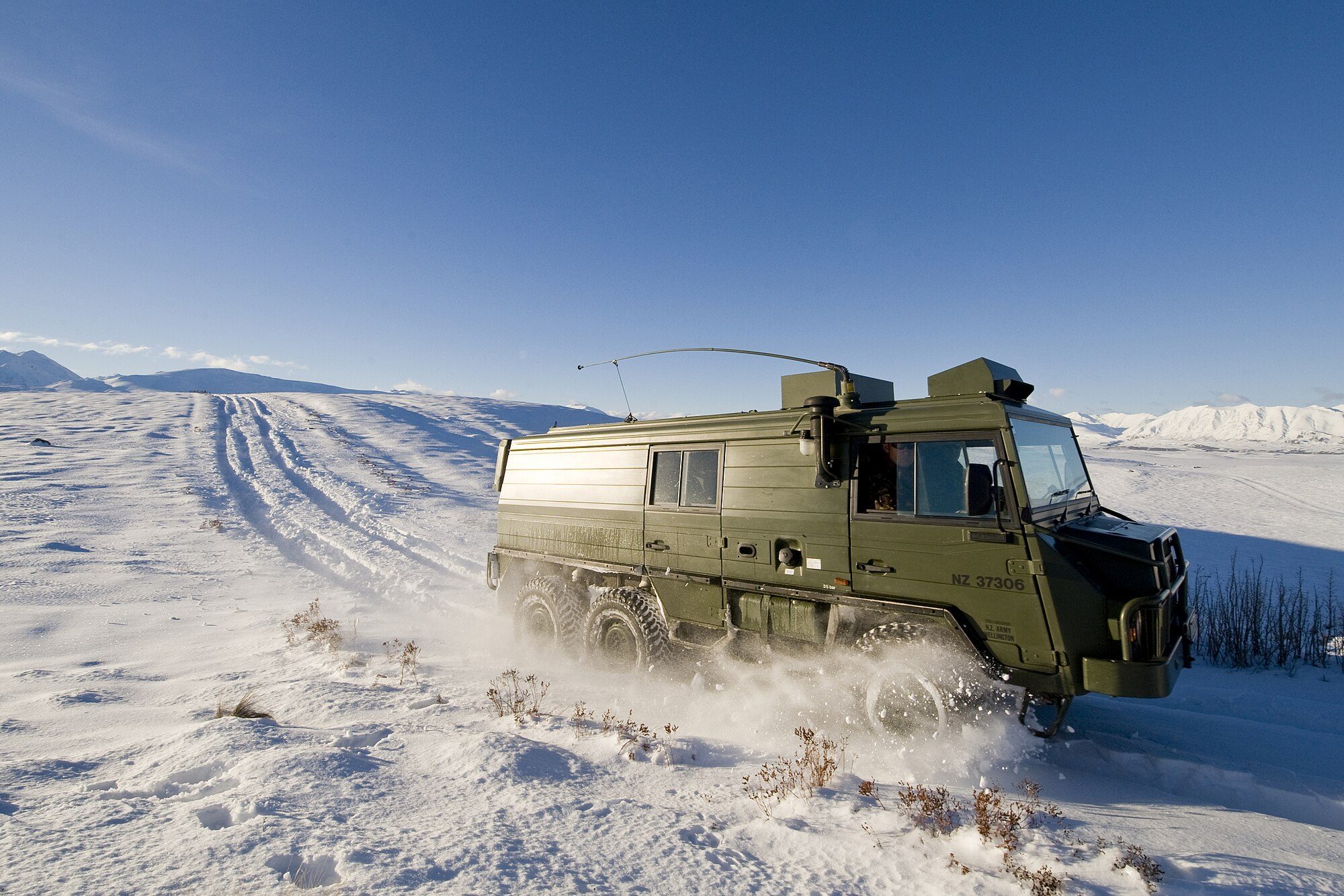 A green New Zealand Army Pinzgauer 718 six-wheeler with a box body ploughing through fresh snow on a hillside near Tekapo