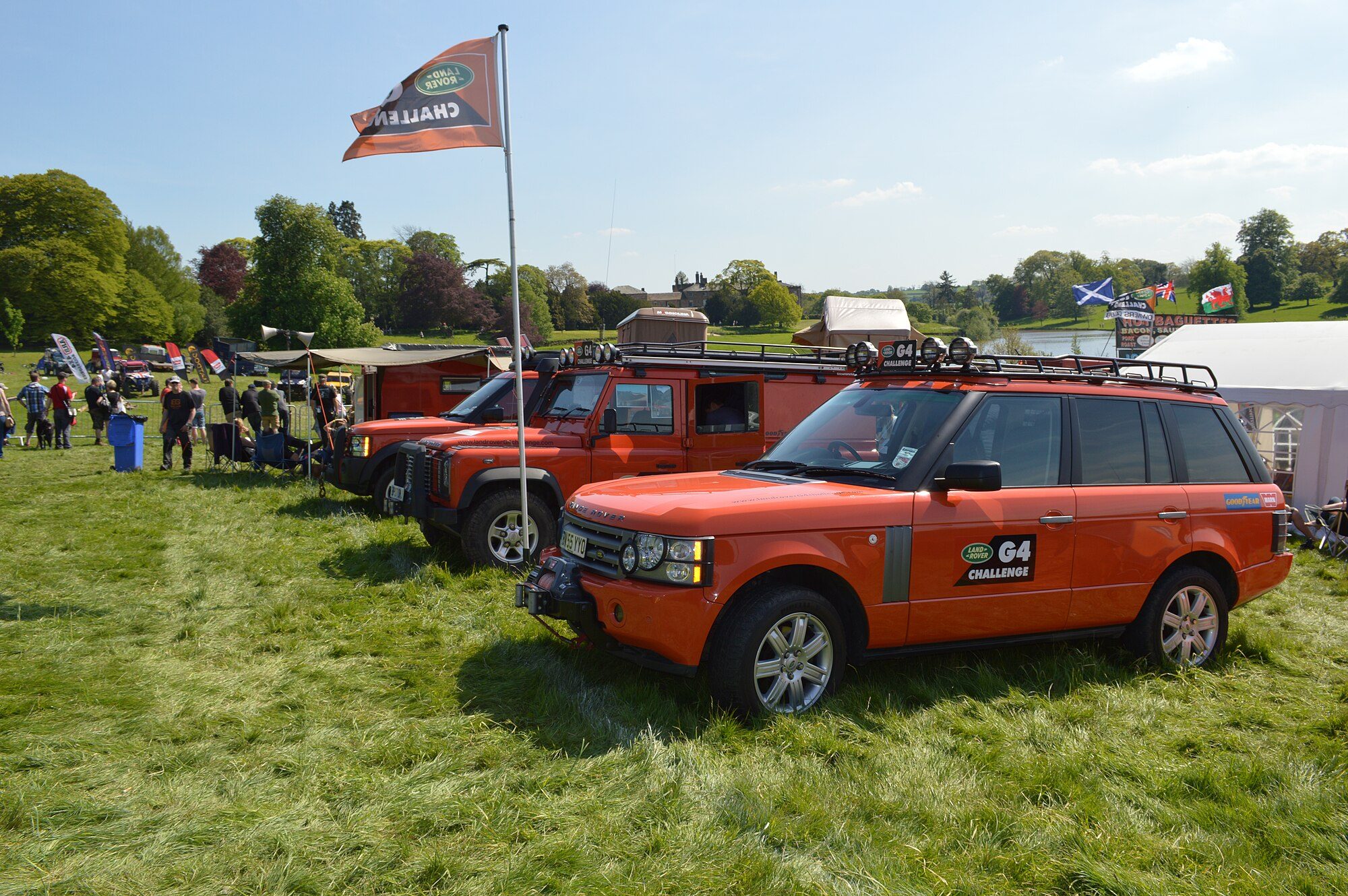 An orange G4 Challenge-edition L322 Range Rover with roof rack parked on grass at a Land Rover off-road gathering