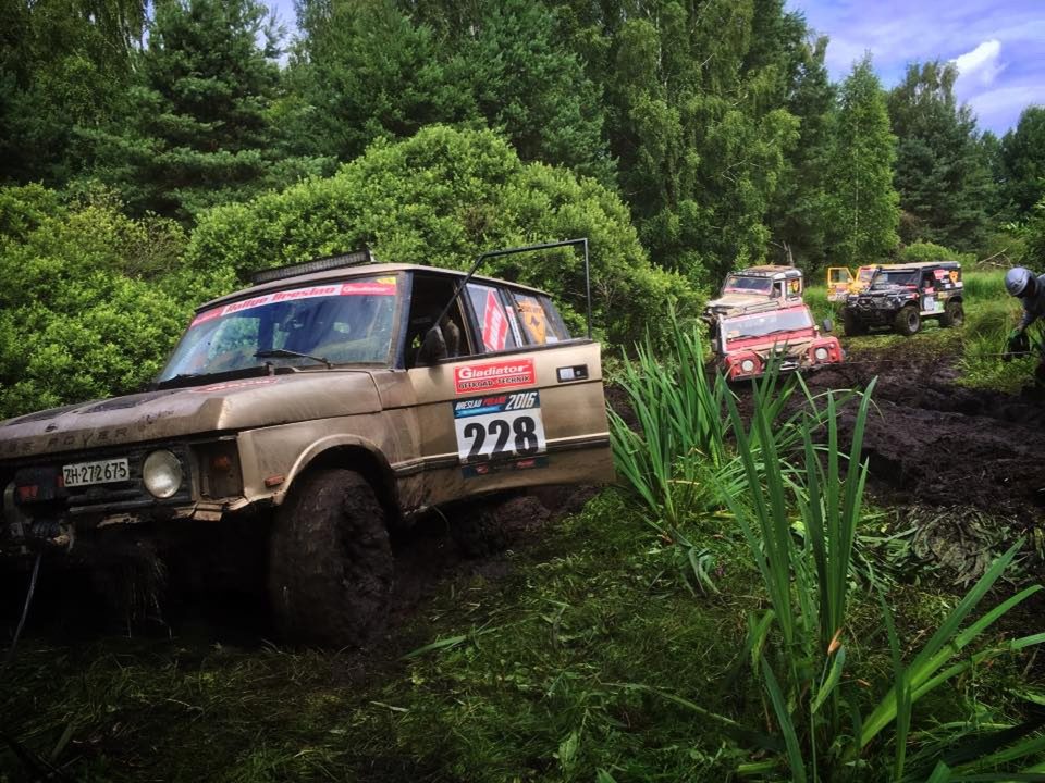 A modified two-door Range Rover Classic rally car in a muddy forest section with other competitors behind