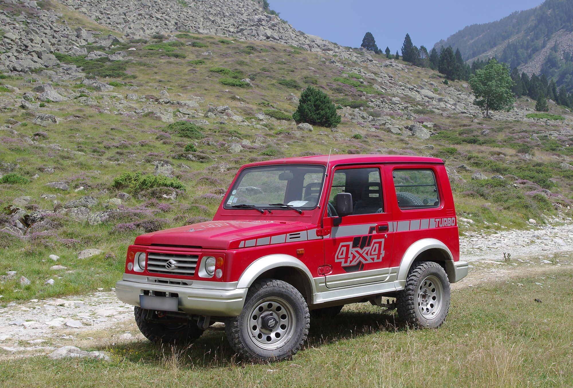 A red Santana-built Suzuki Samurai 1.9 turbodiesel hardtop on a grassy mountain track in the Pyrenees
