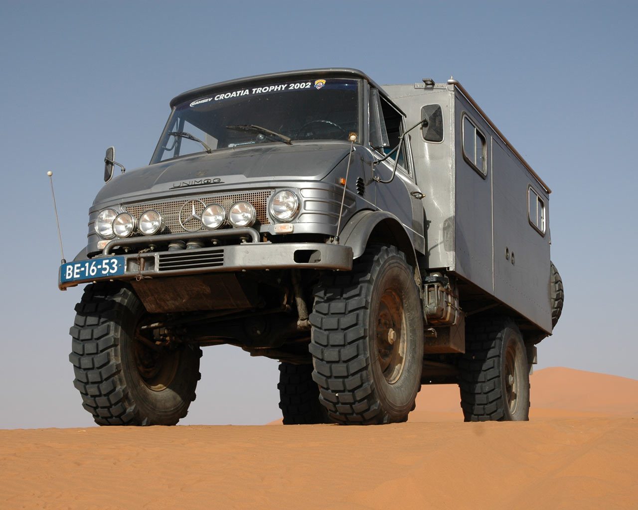 A silver Unimog 404.0 with a 406-style cab and expedition box body on the red sand dunes of Erg Chebbi, Morocco